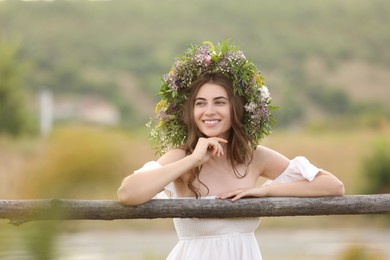 Photo of Young woman wearing wreath made of beautiful flowers near wooden fence