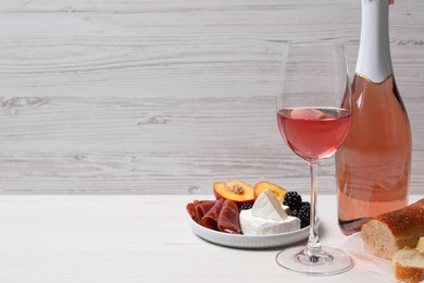 Delicious rose wine and snacks on white wooden table, space for text