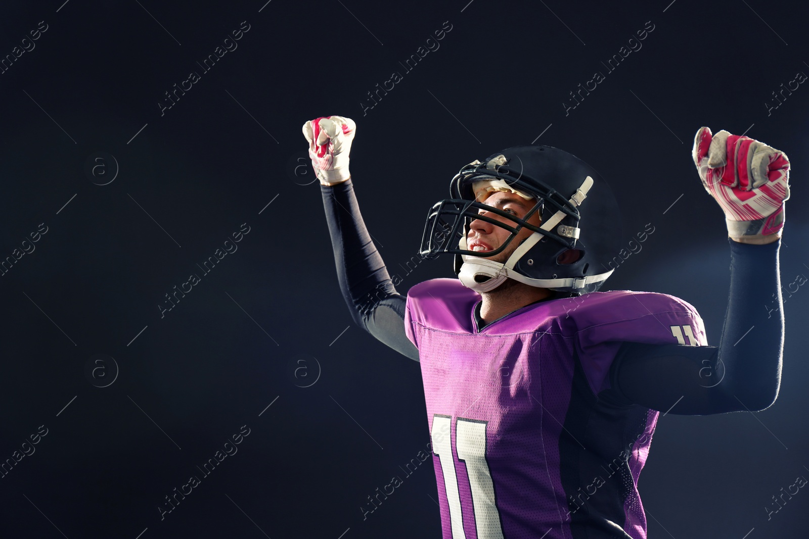 Photo of Happy American football player on dark background. Space for text