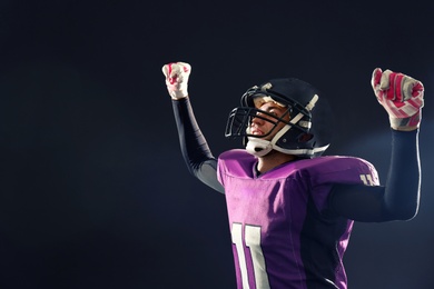 Photo of Happy American football player on dark background. Space for text