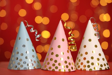 Photo of Beautiful party hats with streamers on red table against blurred festive lights