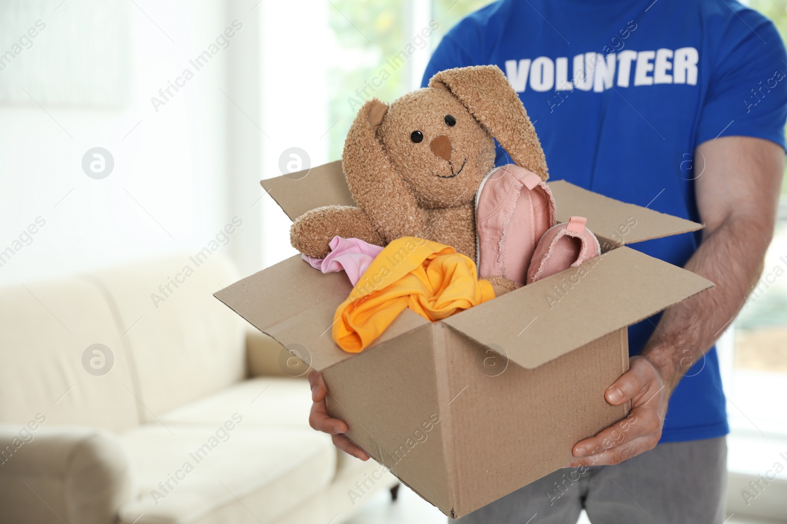 Photo of Male volunteer holding box with donations indoors. Space for text