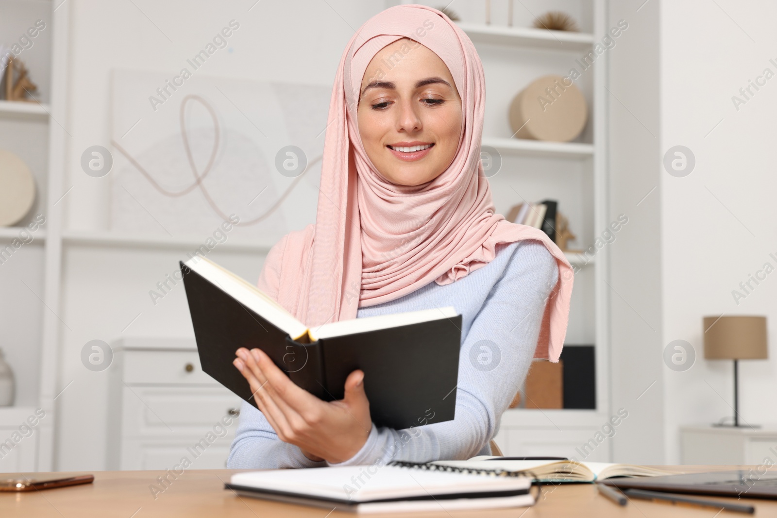 Photo of Muslim woman studying near laptop at wooden table in room