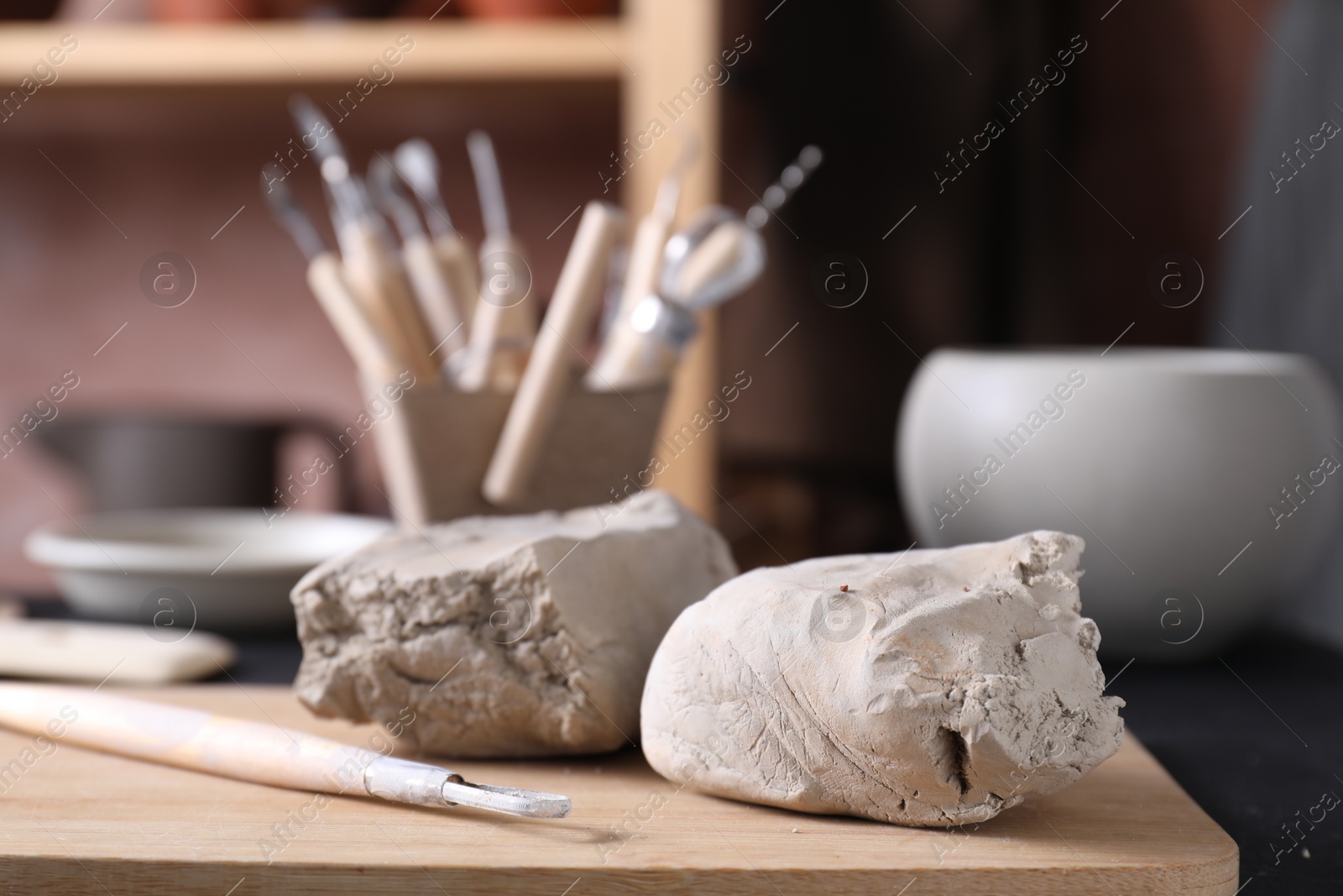 Photo of Clay and set of modeling tools on table in workshop, closeup