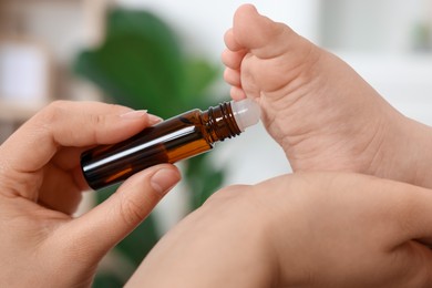 Photo of Mother applying essential oil from roller bottle onto her baby`s heel on blurred background, closeup