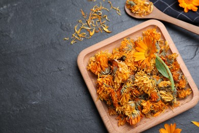 Photo of Dry and fresh calendula flowers on black table, flat lay. Space for text