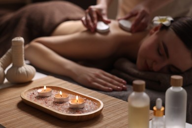 Photo of Spa therapy. Beautiful young woman lying on table during hot stone massage in salon, focus on burning candles