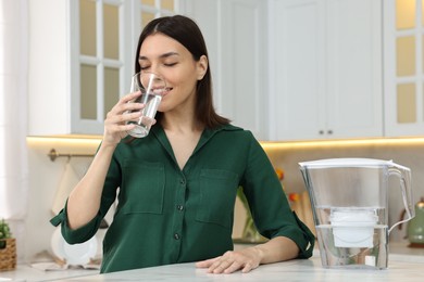 Photo of Woman drinking water and filter jug in kitchen