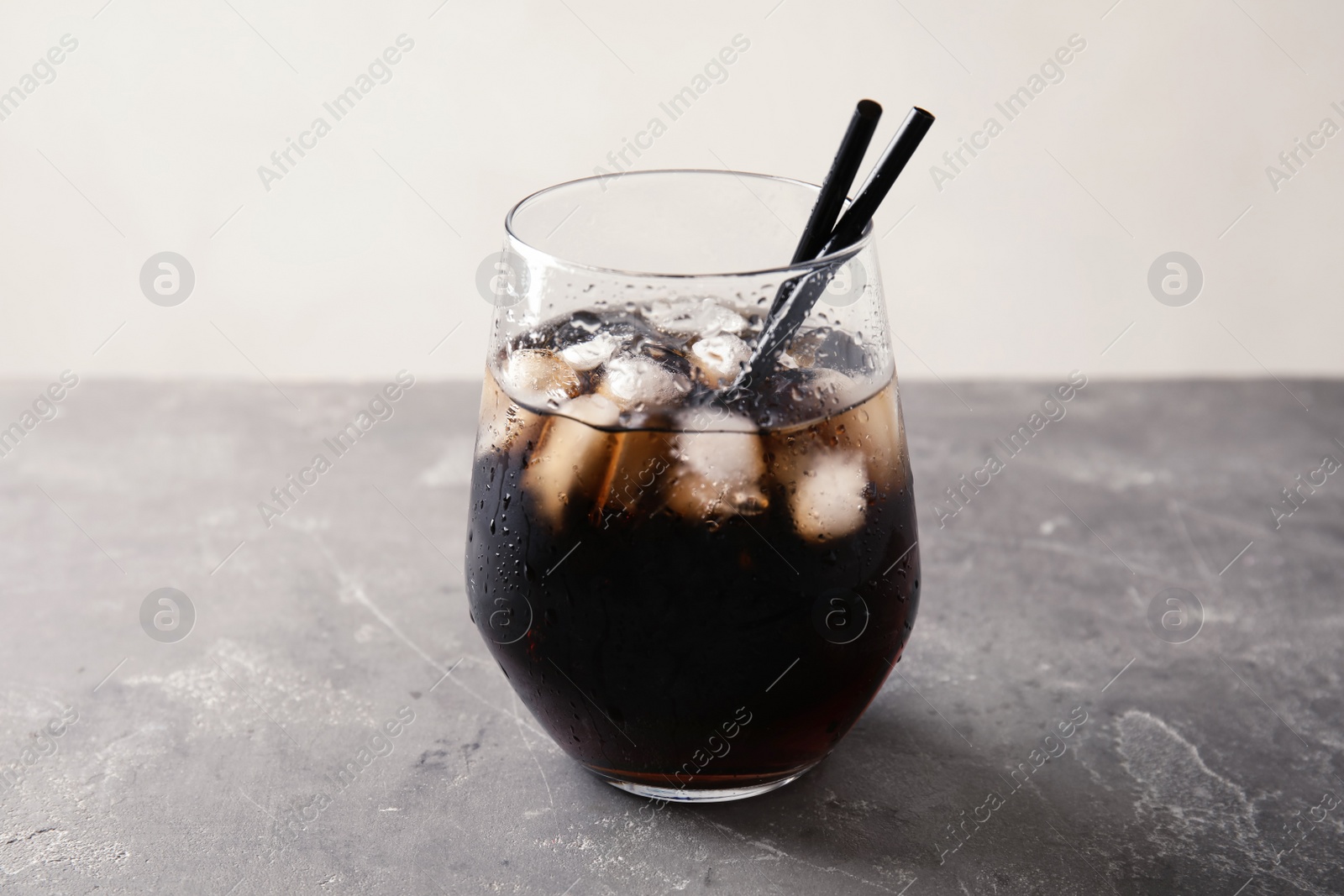 Photo of Glass of refreshing cola with ice on grey table