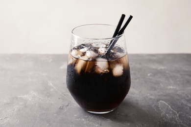 Glass of refreshing cola with ice on grey table