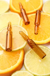 Photo of Skincare ampoules with vitamin C, lemon and orange slices on white background, closeup