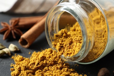 Photo of Jar with dry curry powder on dark table, closeup