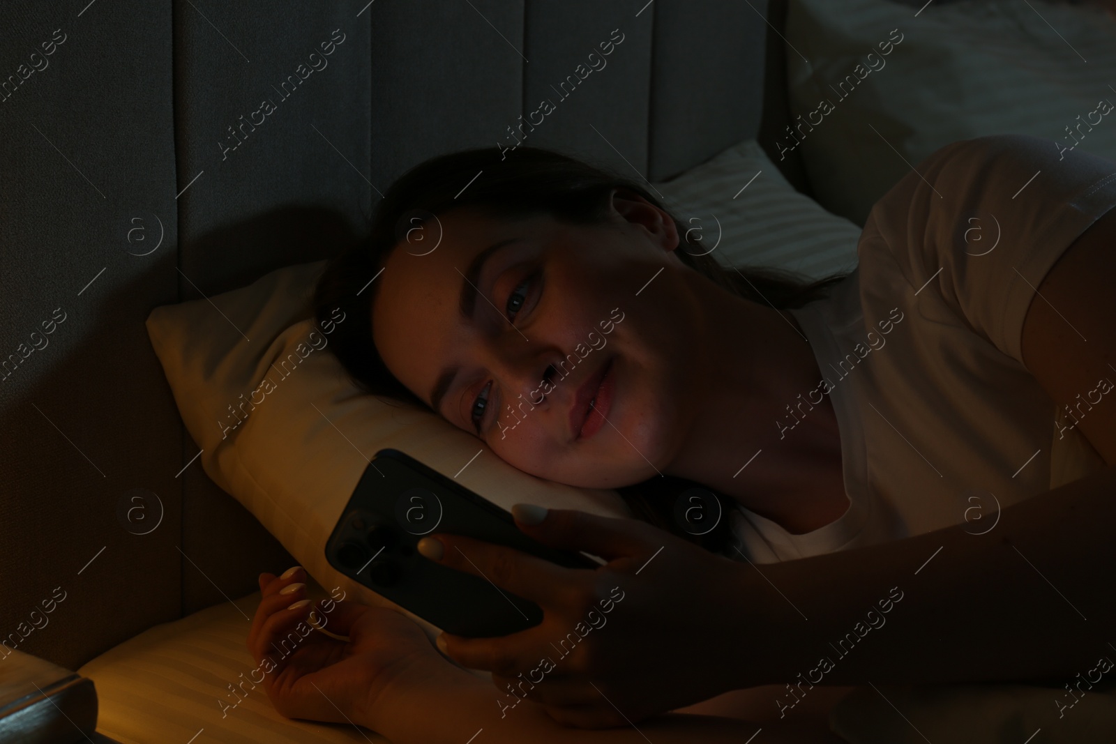 Photo of Woman using smartphone on bed at night. Internet addiction