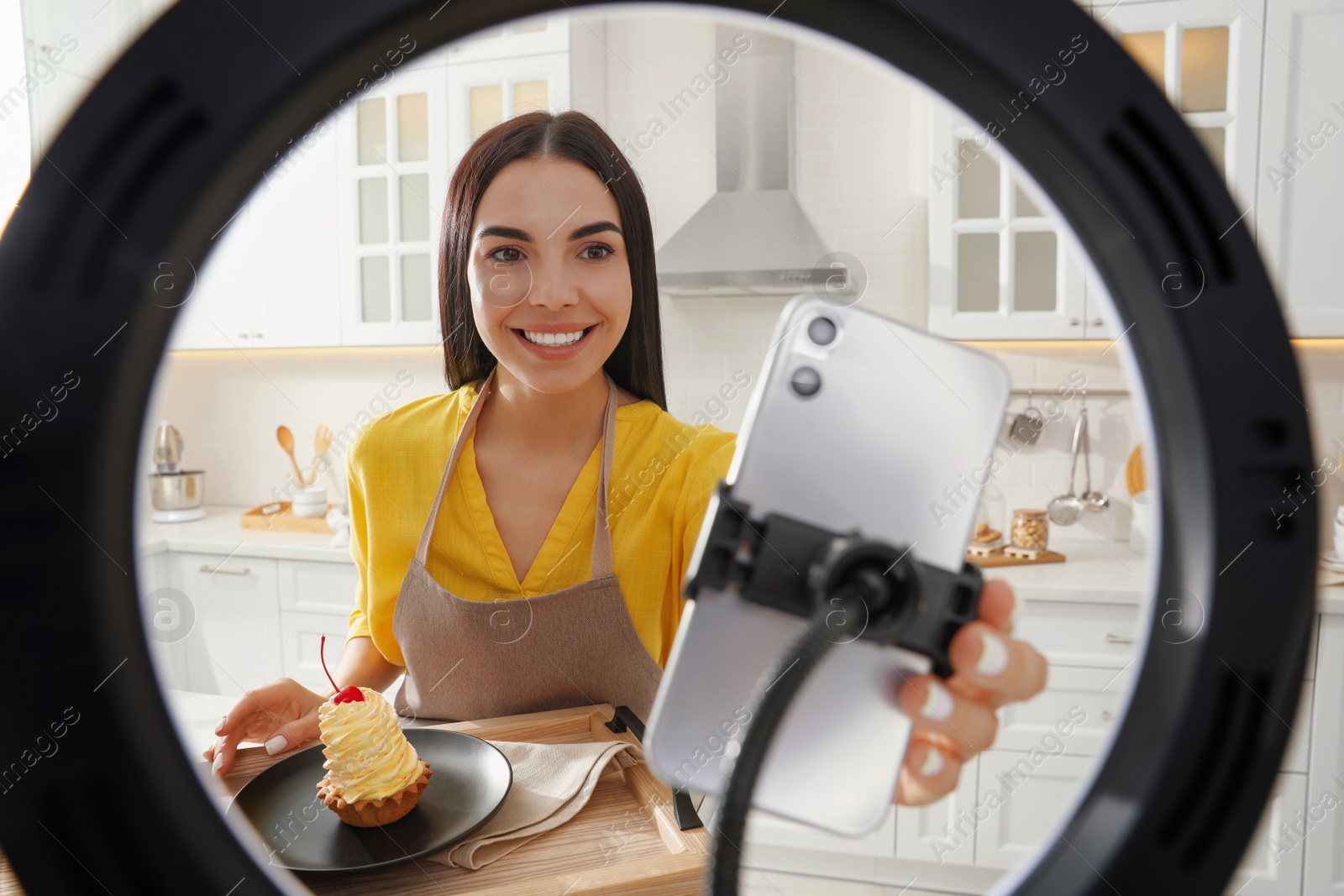 Photo of Blogger preparing for video recording in kitchen at home. Using smartphone and ring lamp