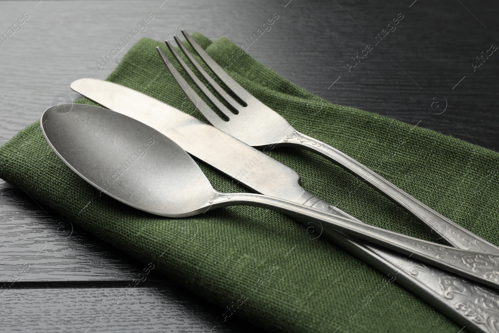 Photo of Stylish setting with cutlery and napkin on black wooden table, closeup