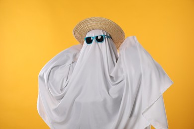 Photo of Person in ghost costume, sunglasses and straw hat on yellow background