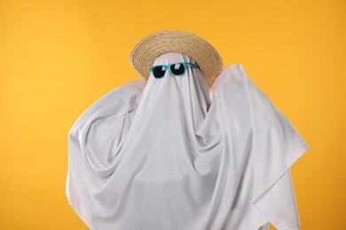 Person in ghost costume, sunglasses and straw hat on yellow background