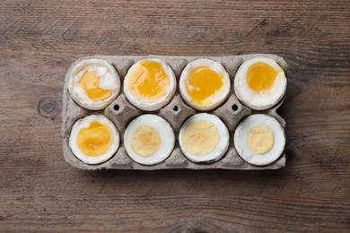 Boiled chicken eggs of different readiness stages in carton on wooden table, top view