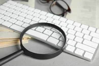 Photo of Magnifying glass, keyboard and stack of newspapers on grey table, closeup. Job search concept