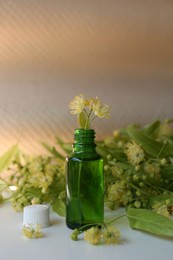 Bottle of essential oil with linden blossoms on white table