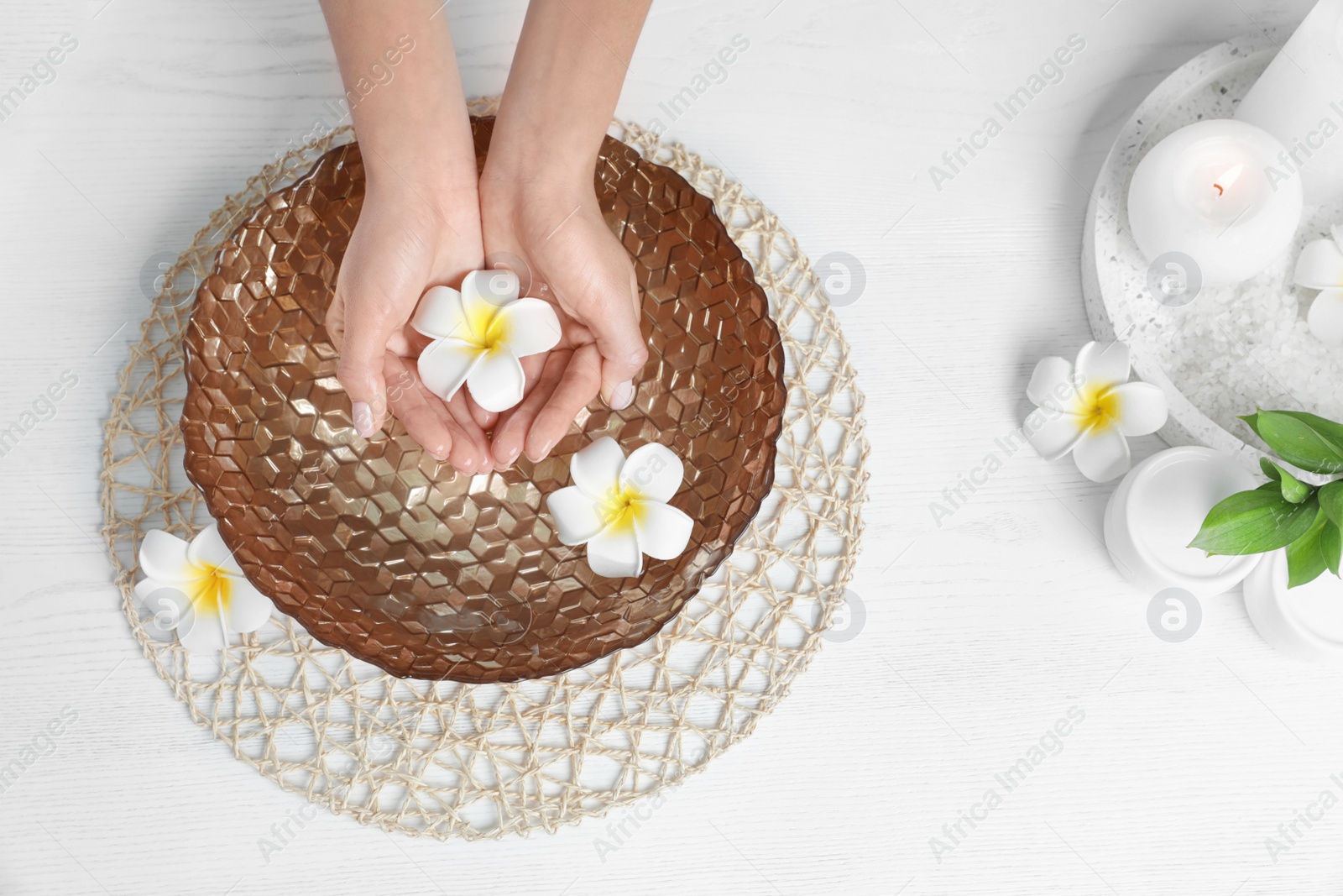 Photo of Woman soaking her hands in bowl with water and flowers on wooden table, top view. Spa treatment