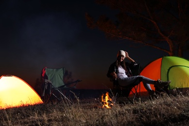 Young woman sitting near bonfire at night. Camping season