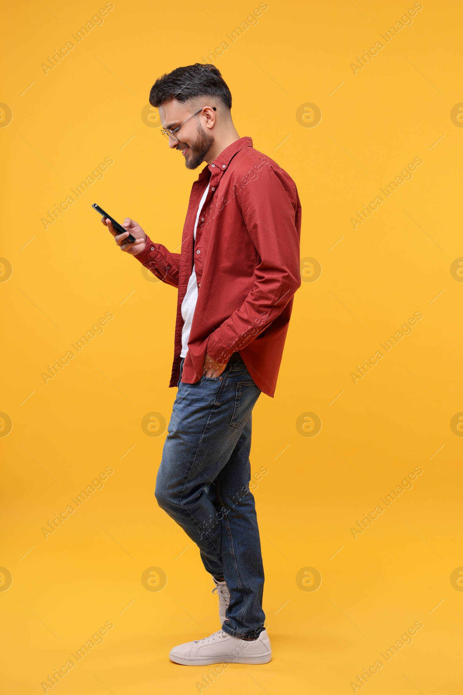 Photo of Happy young man using smartphone on yellow background