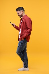 Happy young man using smartphone on yellow background