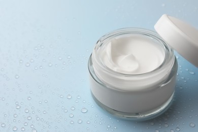 Photo of Jar of face cream on light blue surface covered with water drops, space for text