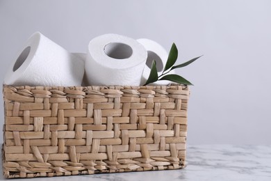 Photo of Toilet paper rolls and green leaves in wicker basket on white marble table, space for text