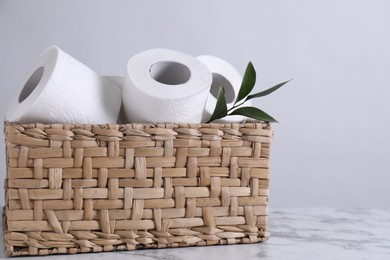 Toilet paper rolls and green leaves in wicker basket on white marble table, space for text