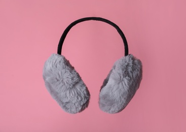 Fluffy earmuffs on pink background. Stylish winter accessory