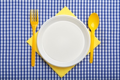 Photo of Table setting with plastic dishware on plaid fabric, flat lay