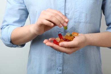 Photo of Woman holding colorful jelly bears on light background, closeup