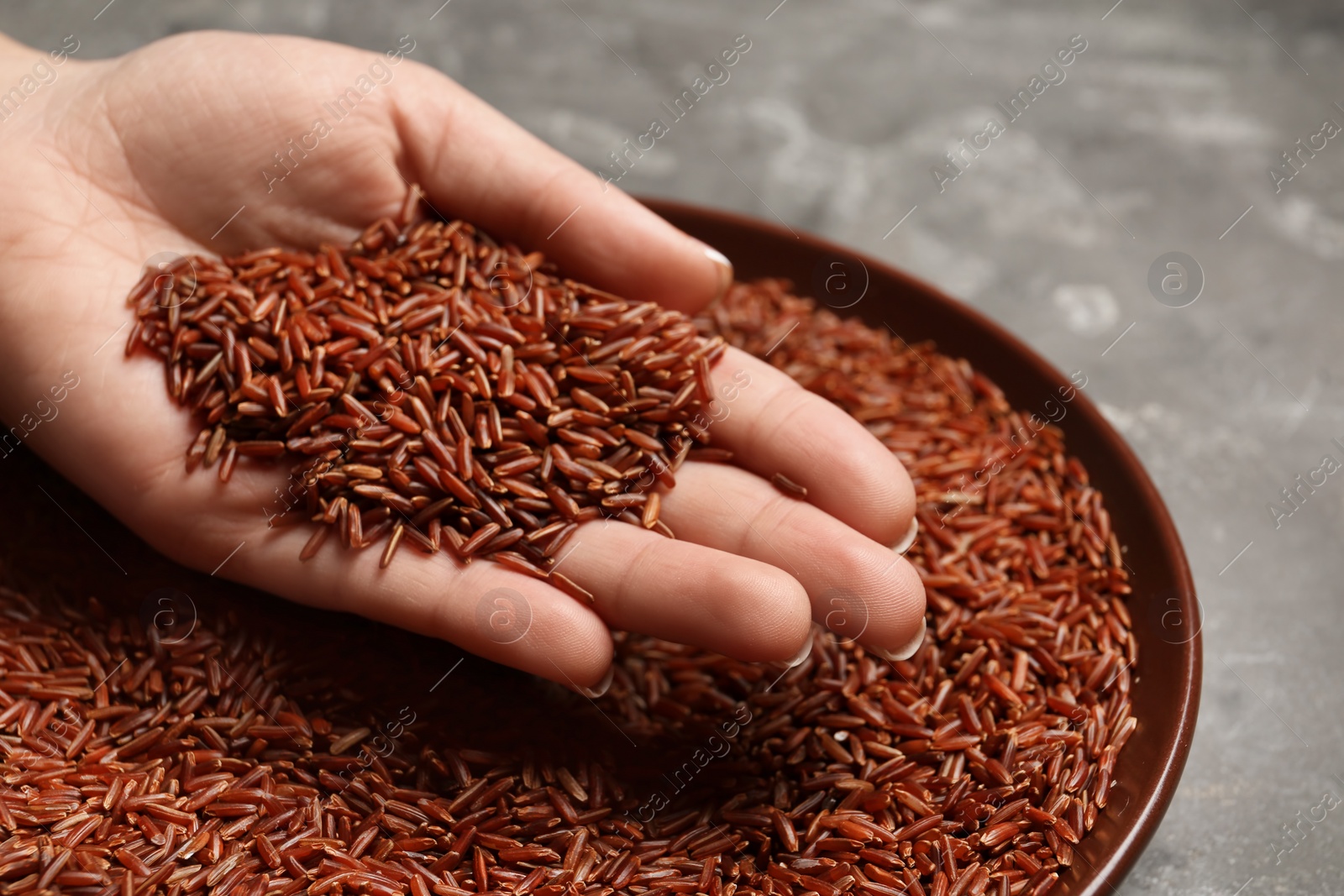Photo of Woman holding grains near plate with brown rice on table, closeup