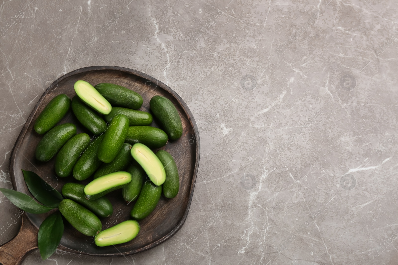 Photo of Fresh seedless avocados with green leaves on grey table, flat lay. Space for text