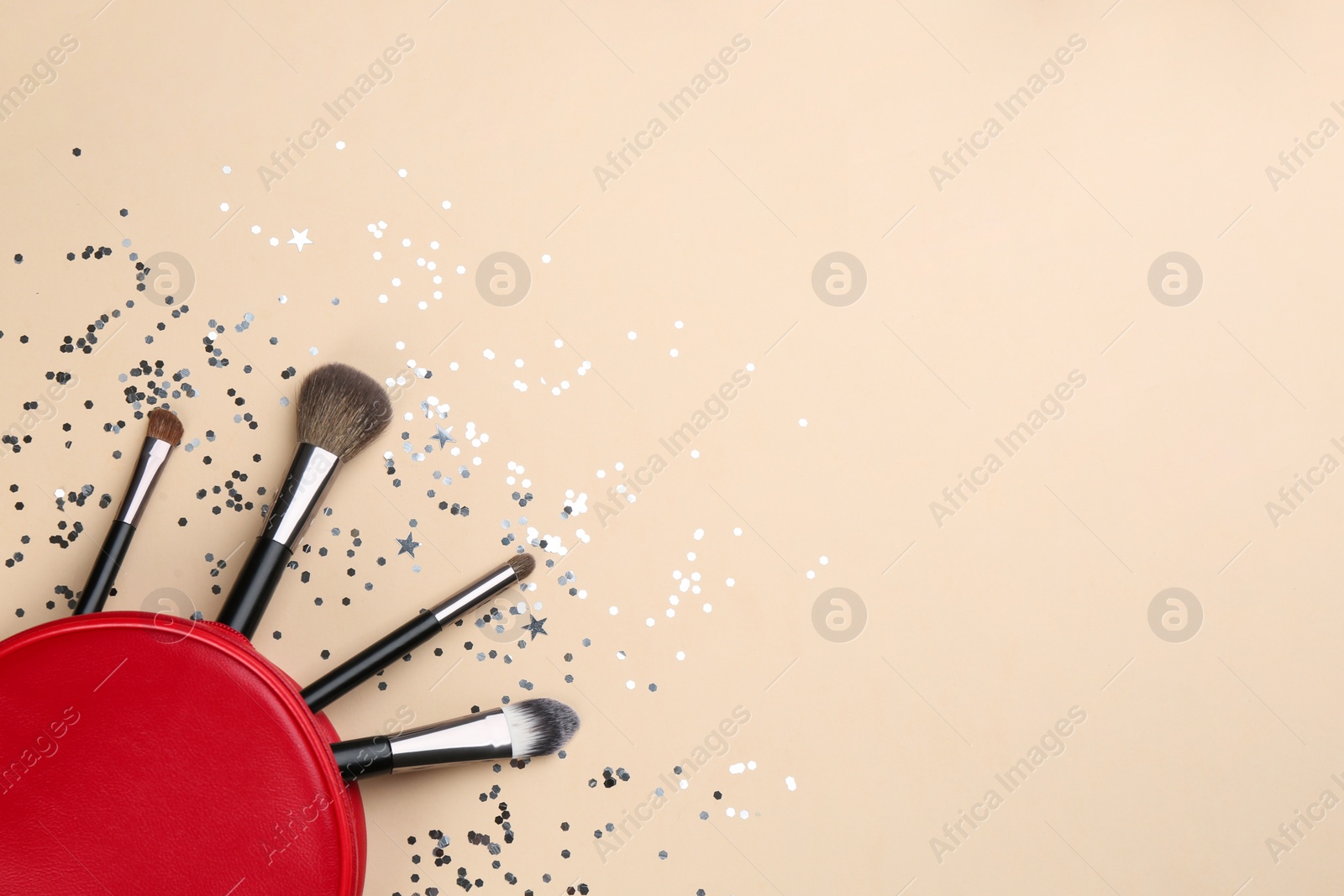 Photo of Different makeup brushes, case and shiny confetti on beige background, flat lay. Space for text