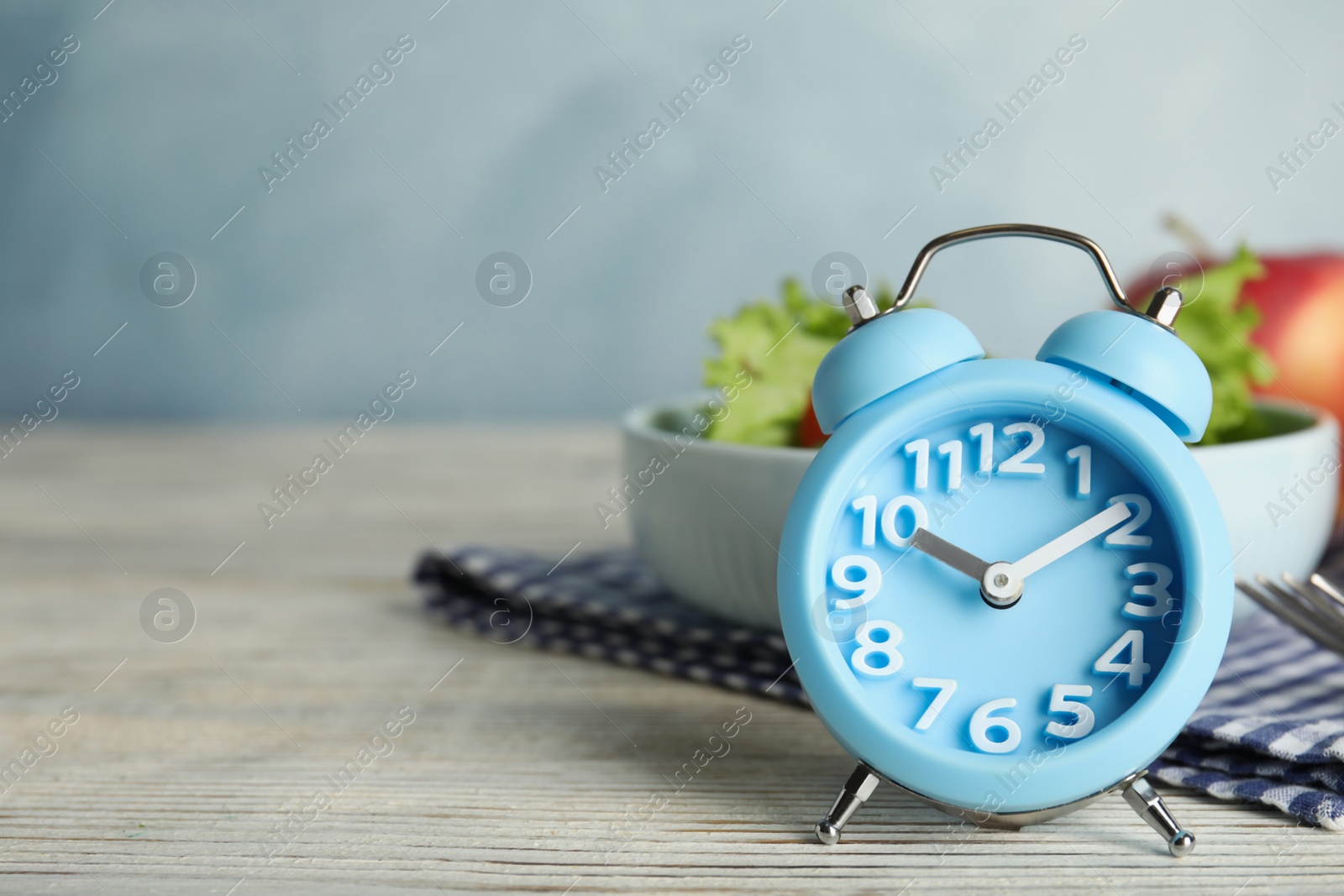 Photo of Alarm clock and healthy food on white wooden table, space for text. Meal timing concept