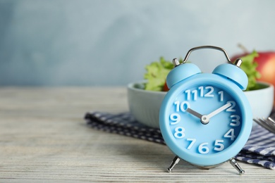 Photo of Alarm clock and healthy food on white wooden table, space for text. Meal timing concept