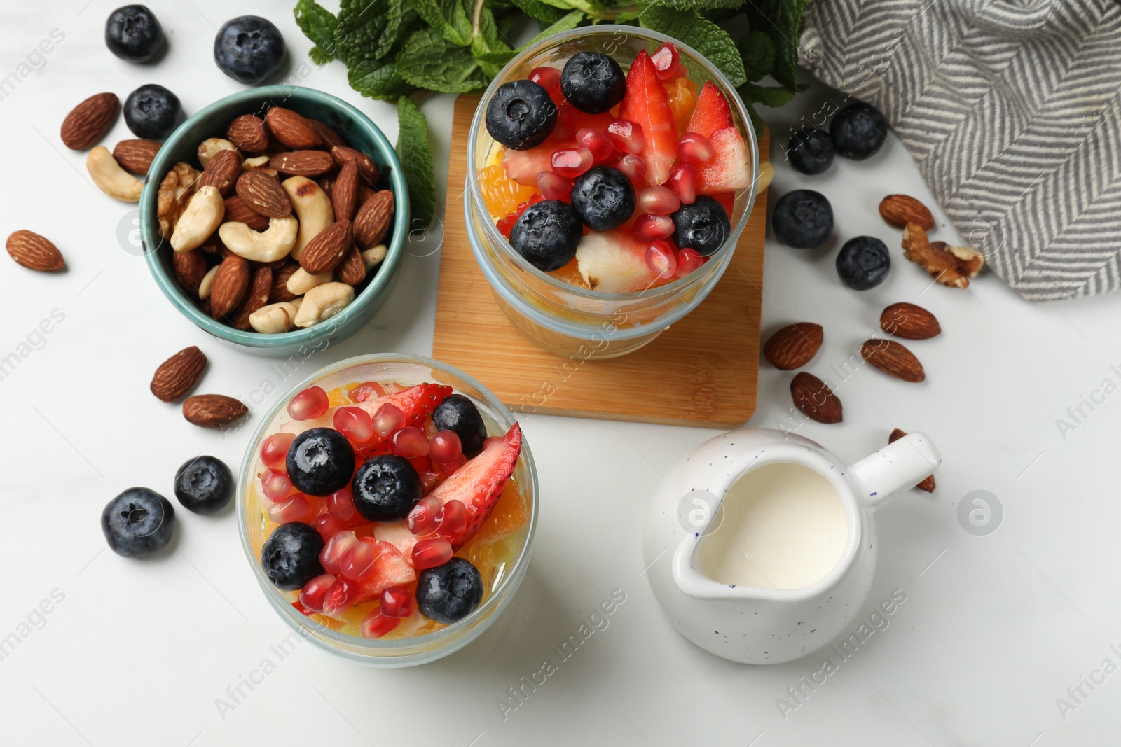 Photo of Delicious fruit salad, fresh berries, mint and nuts on white marble table, flat lay
