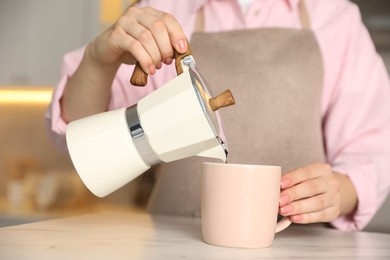 Photo of Woman pouring aromatic coffee from moka pot into cup at white marble table, closeup