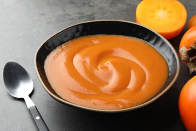 Photo of Delicious persimmon jam in bowl served on gray table, closeup