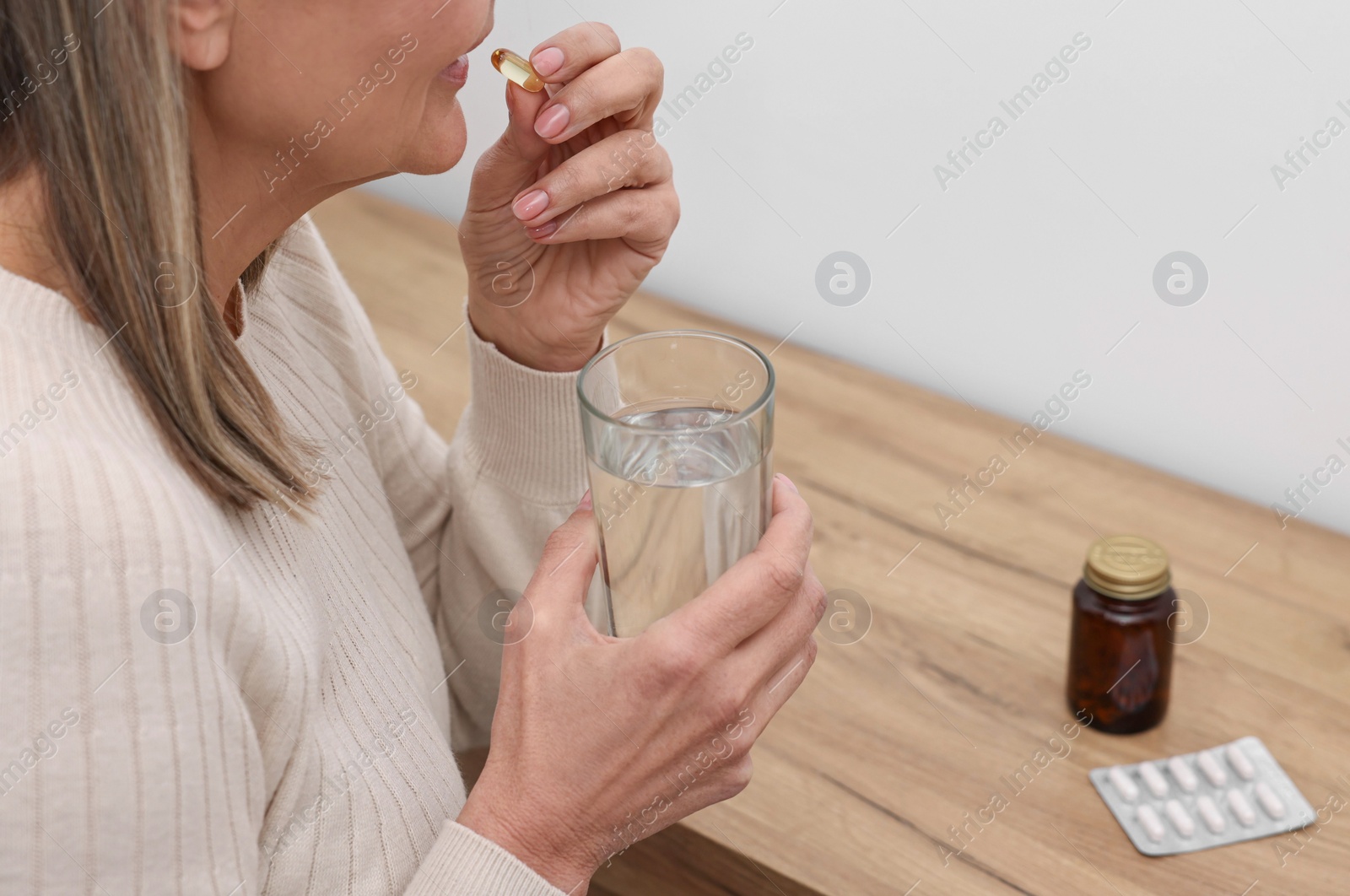 Photo of Woman taking vitamin pill at table indoors, closeup. Space for text