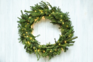 Photo of Beautiful Christmas wreath with festive lights on white wooden background, top view