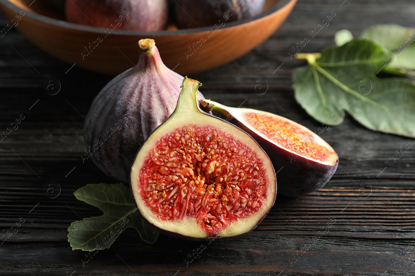 Photo of Fresh ripe figs with leaves on wooden table. Tropical fruit