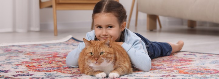 Smiling little girl and cute ginger cat on carpet at home. Banner design