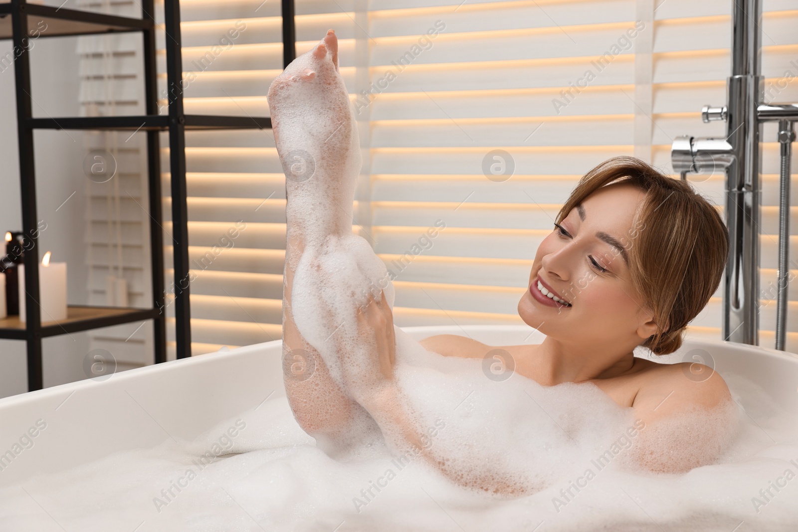 Photo of Happy woman taking bath with foam in tub indoors