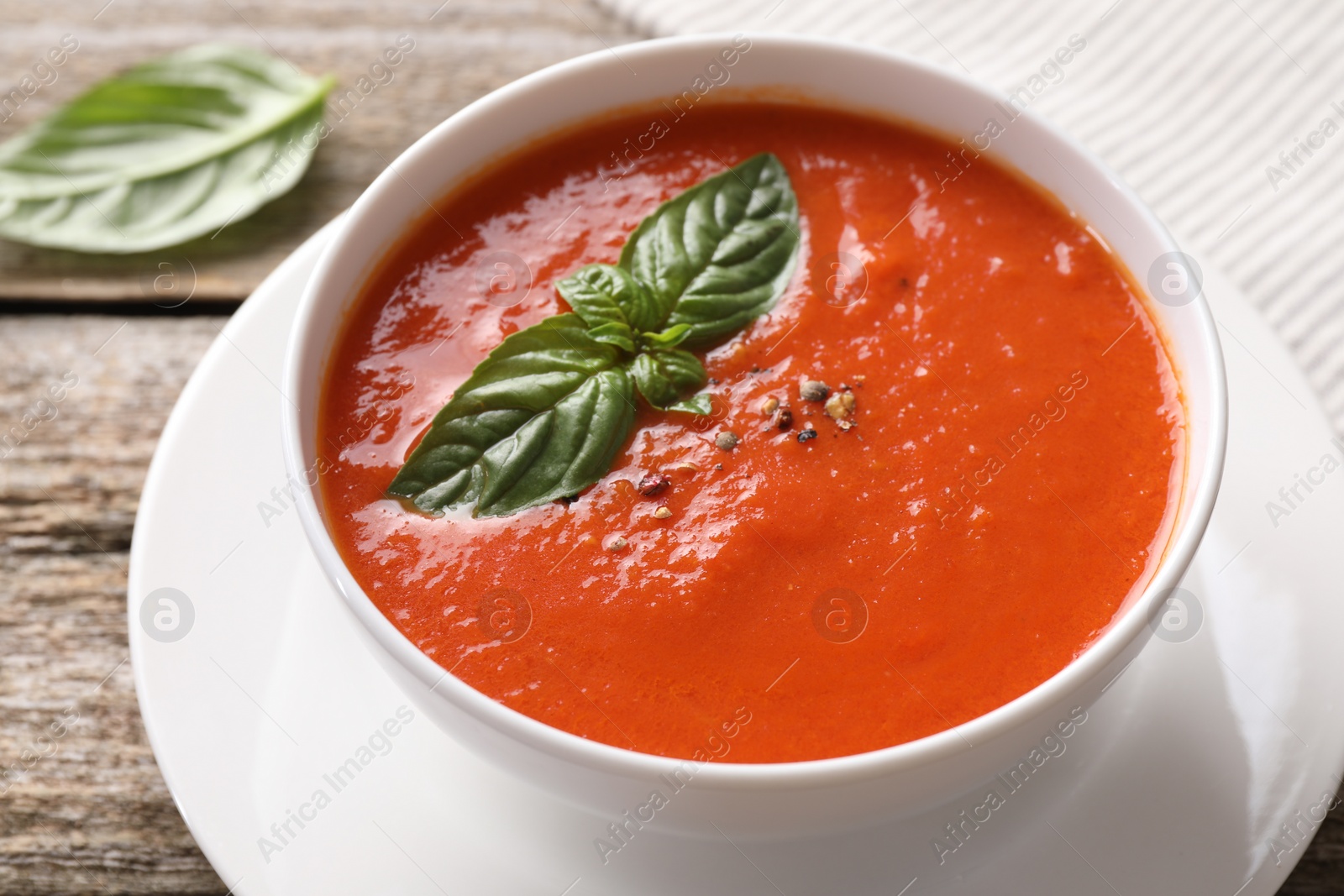 Photo of Delicious tomato soup with basil and spices on wooden table, closeup