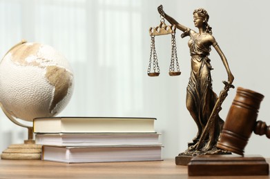 Photo of Figure of Lady Justice, gavel, books and globe on wooden table indoors, space for text. Symbol of fair treatment under law