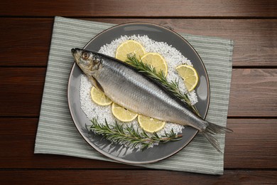 Photo of Delicious salted herring, rosemary, salt and lemon on wooden table, top view